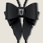 Black Leather Bow with Central Brand Logo on Beige Background