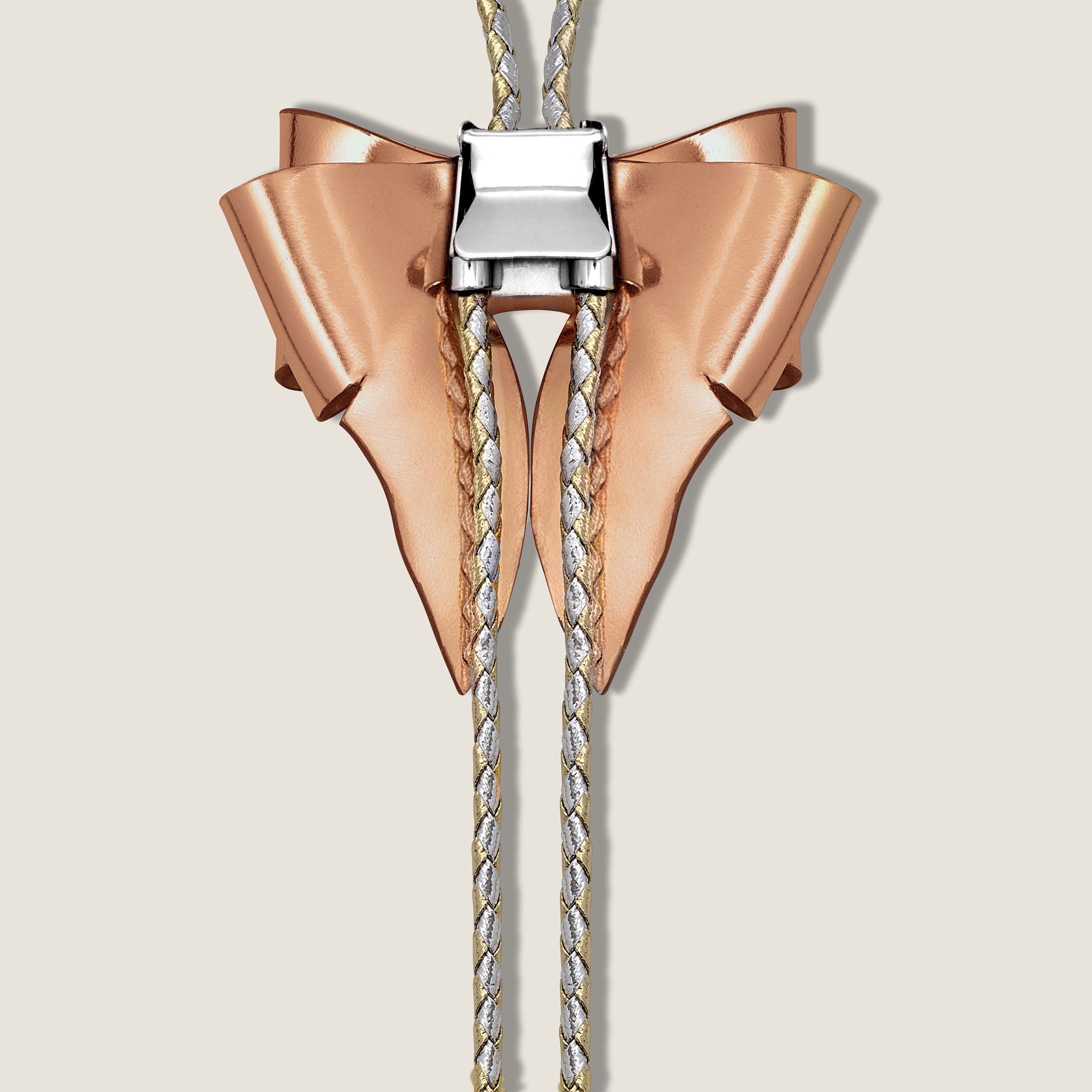 Rose gold and silver bow-shaped bolo tie on a beige background