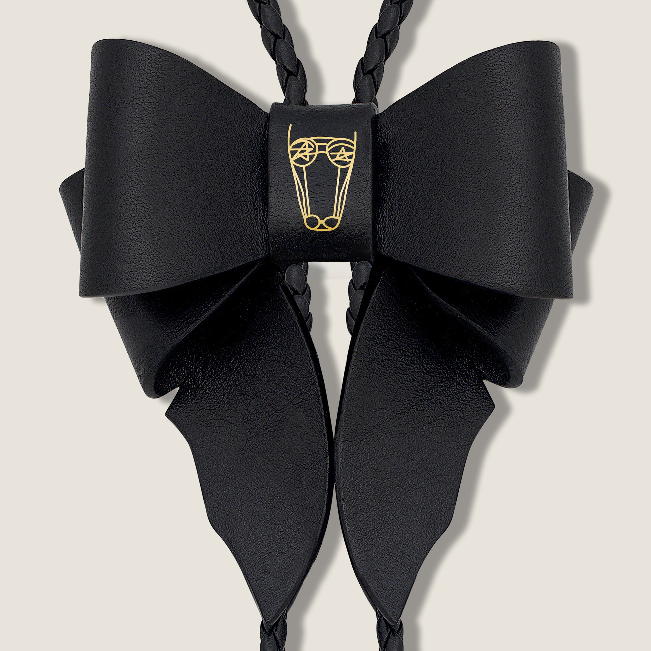 Black Leather Bow with Gold Brand Logo on Beige Background