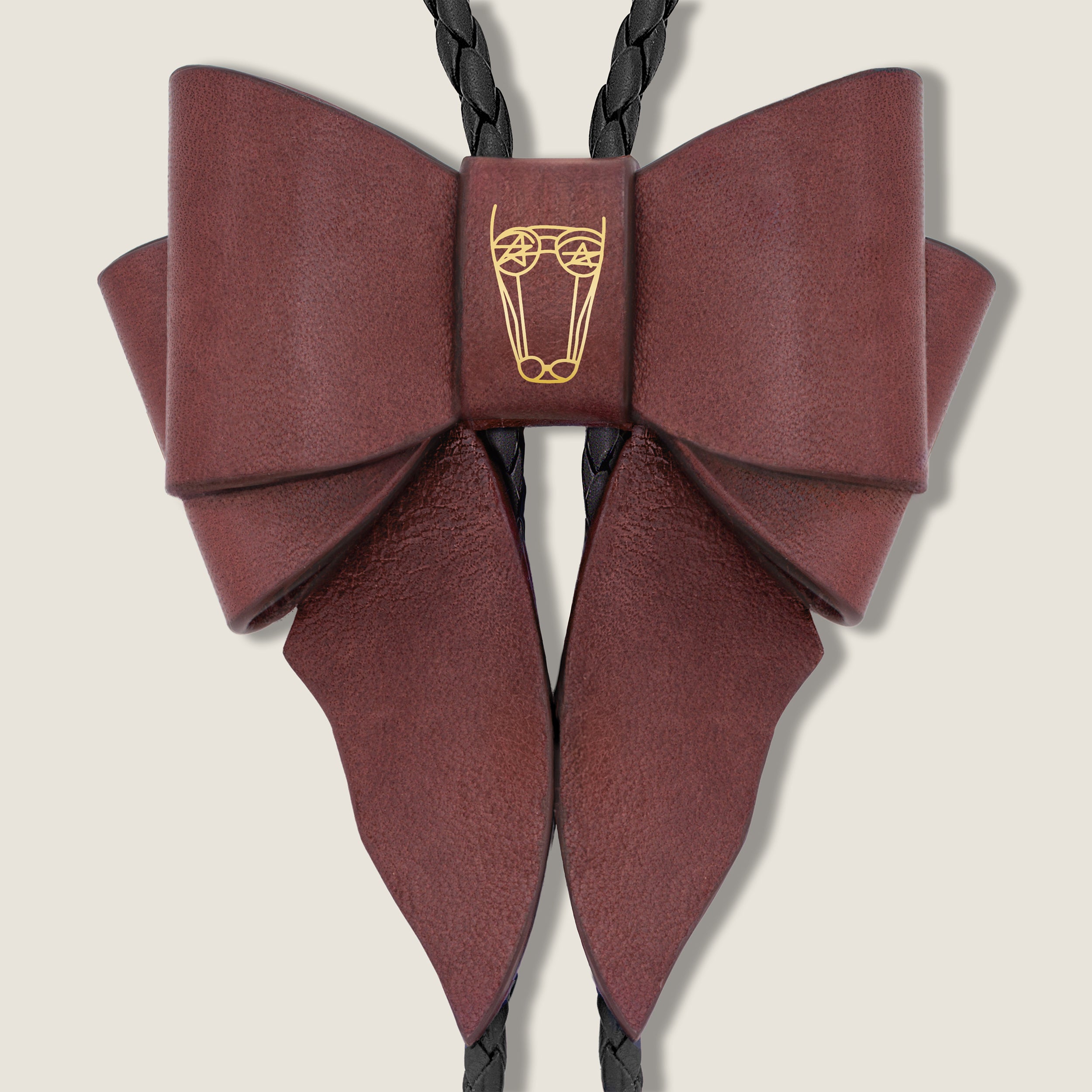 Burgundy leather bow with a central brand emblem on a beige background