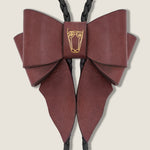 Burgundy leather bow with a central brand emblem on a beige background