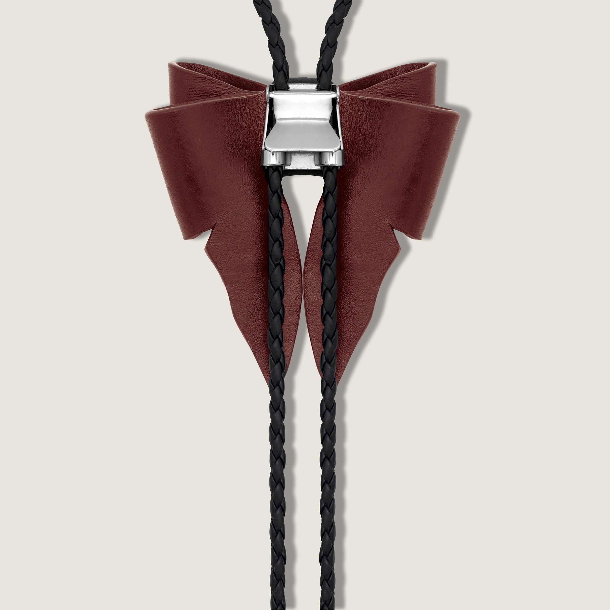 Bolo tie with maroon leather bow and black braided cord on a beige background