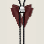 Bolo tie with maroon leather bow and black braided cord on a beige background
