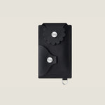 Black cardholder with scallop edge flap design and silver snaps with d-ring for removable chain on a beige background