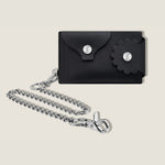 Black leather wallet with floral flap design and removable chain on a beige background