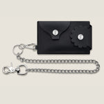 Black wallet with floral flap design and detachable chain on a beige background