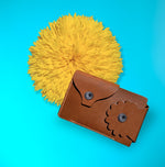 Marrs Makers Cognac Brown Leather Wallet. Bright turquoise background color with large sunflower in this product shot.